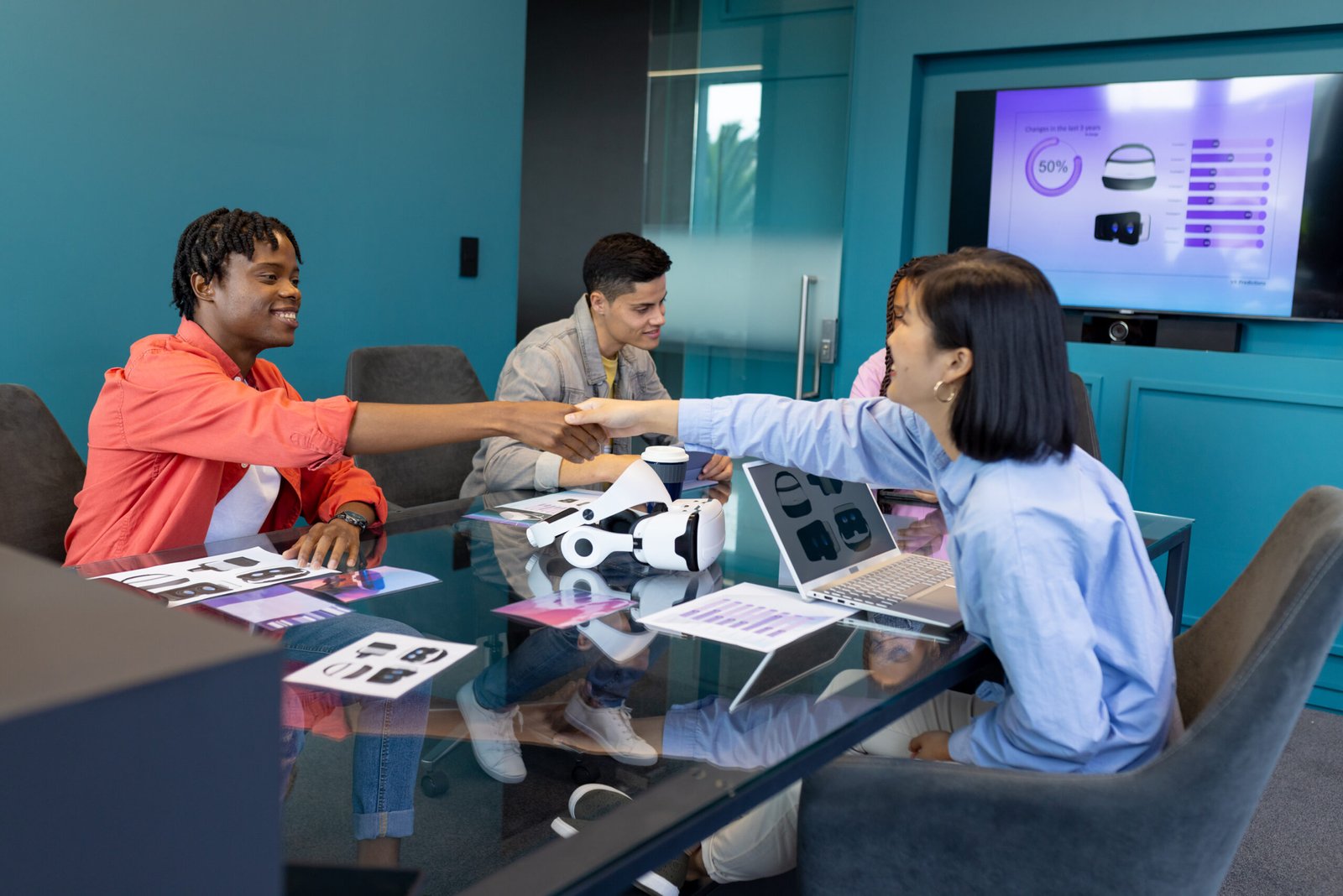 Business team discuss VR, startup, teamwork, and collaboration while shaking hands. They are in modern conference room with VR headsets and presentation on screen, unaltered