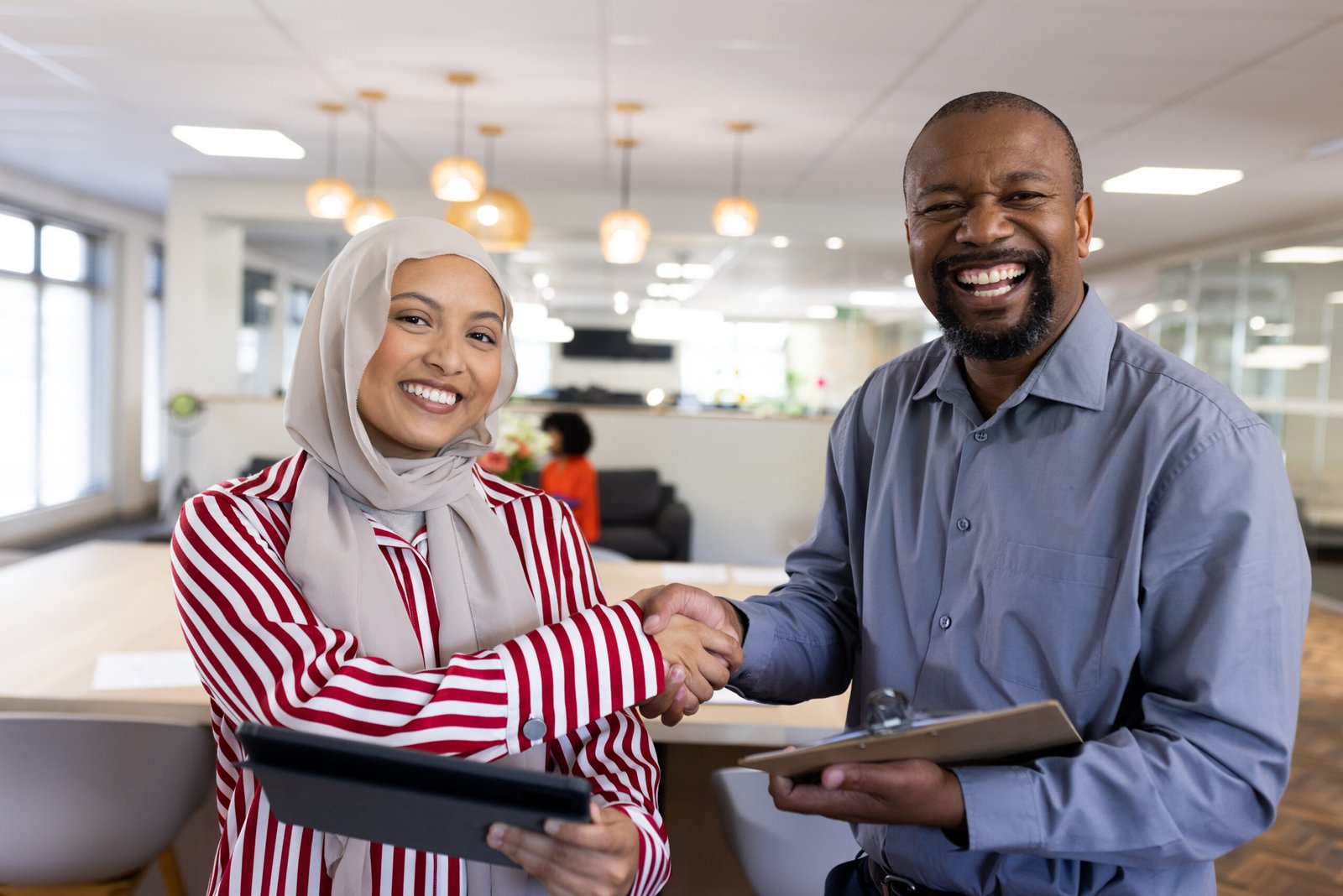 Happy diverse female and male business people shaking hands and looking at camera in office. Business, corporation, working in office and cooperation concept.